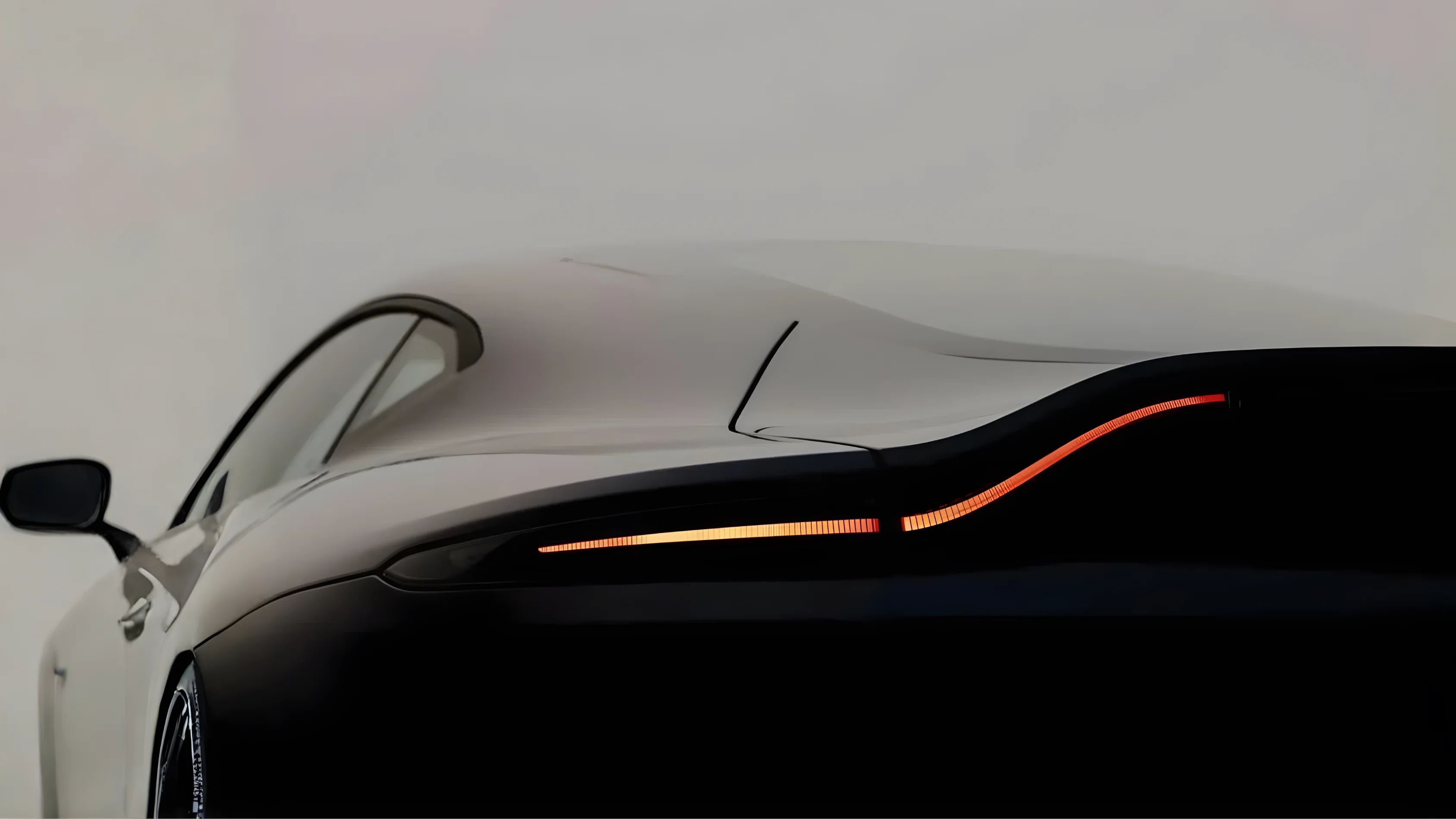 Rear side view of a sleek white sports car with illuminated curved tail light on a light gray background.