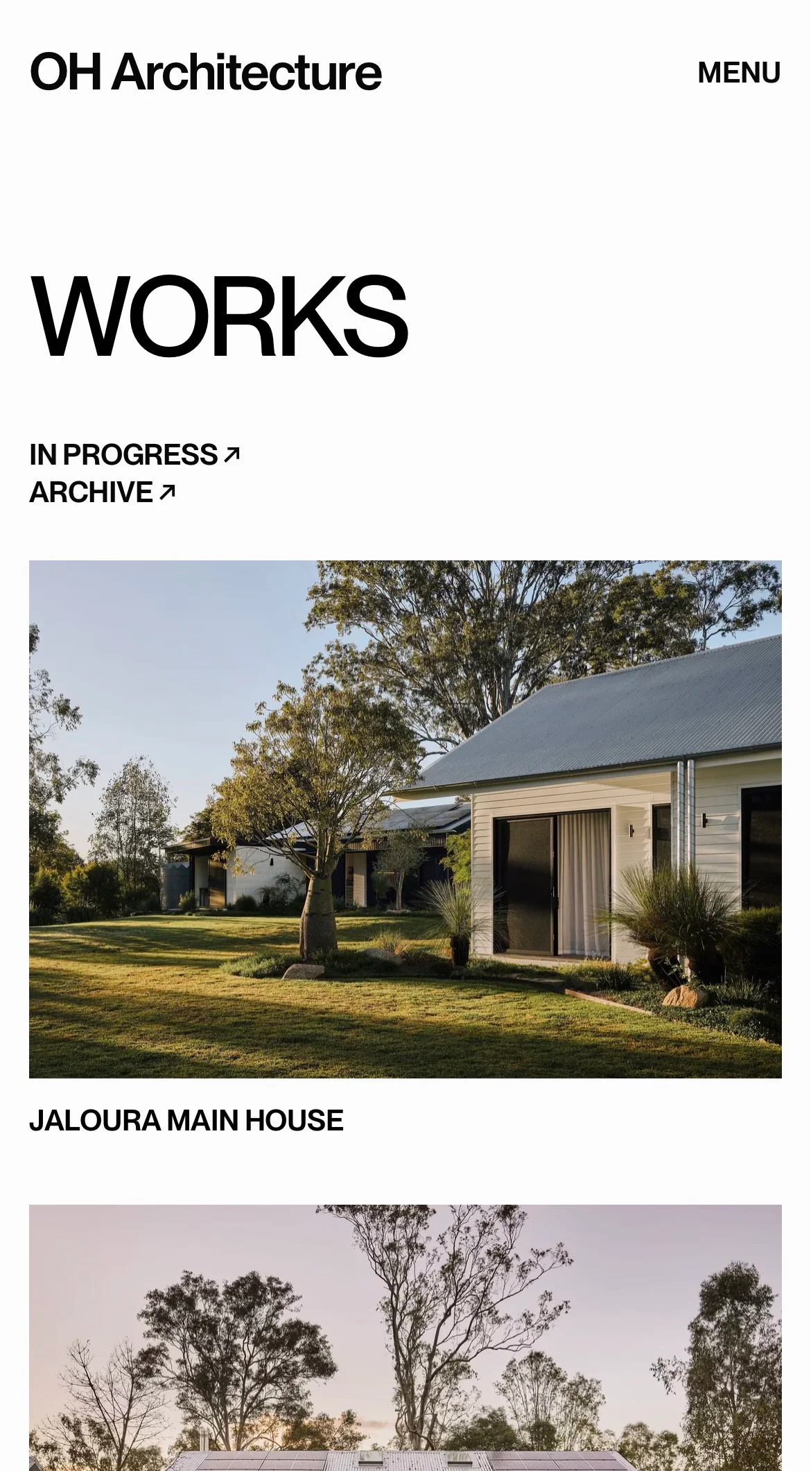 Modern single-story house with white siding, metal roof, and landscaped lawn surrounded by tall trees.
