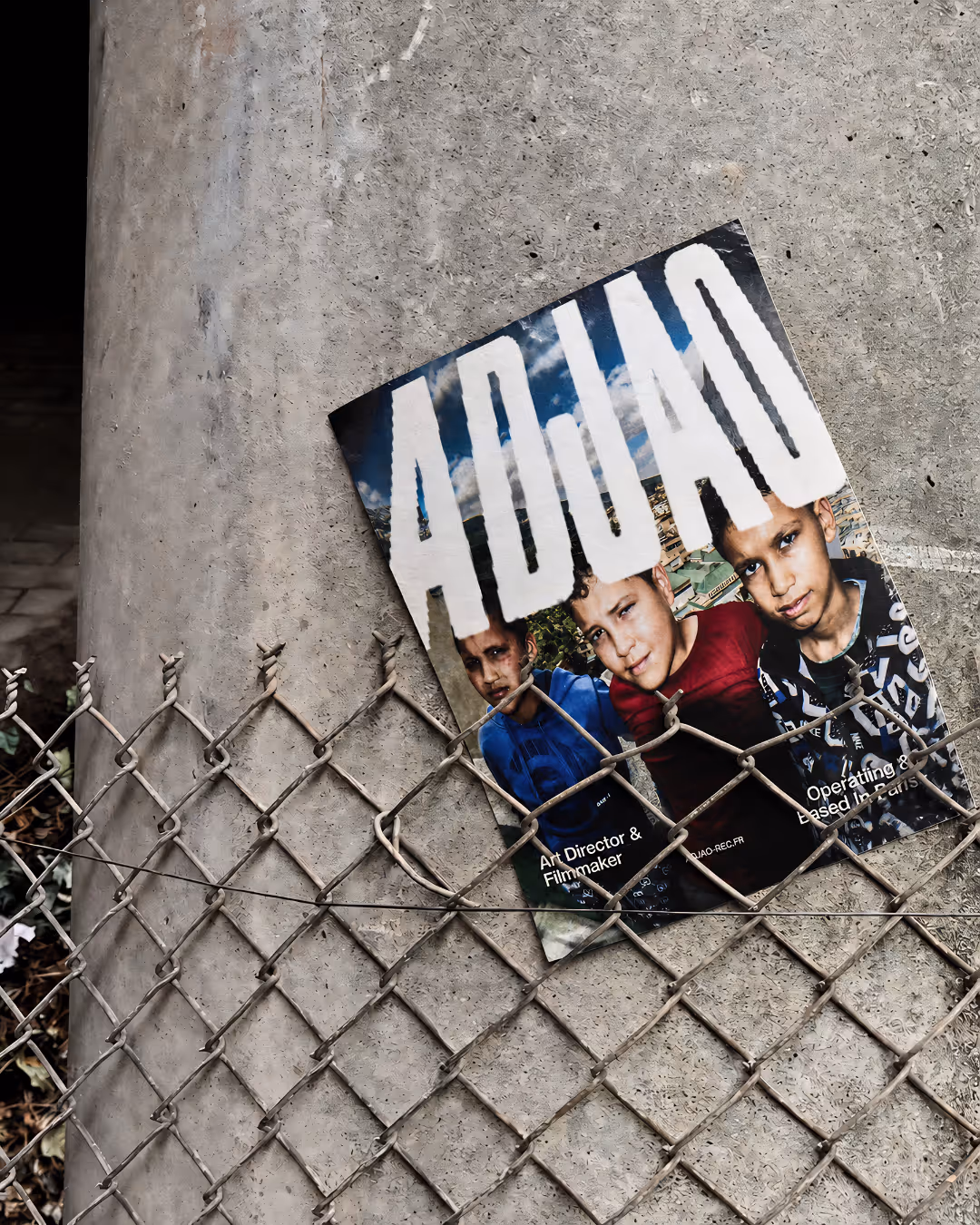 Magazine avec photo de trois garçons collé sur un poteau en béton derrière une clôture en métal.