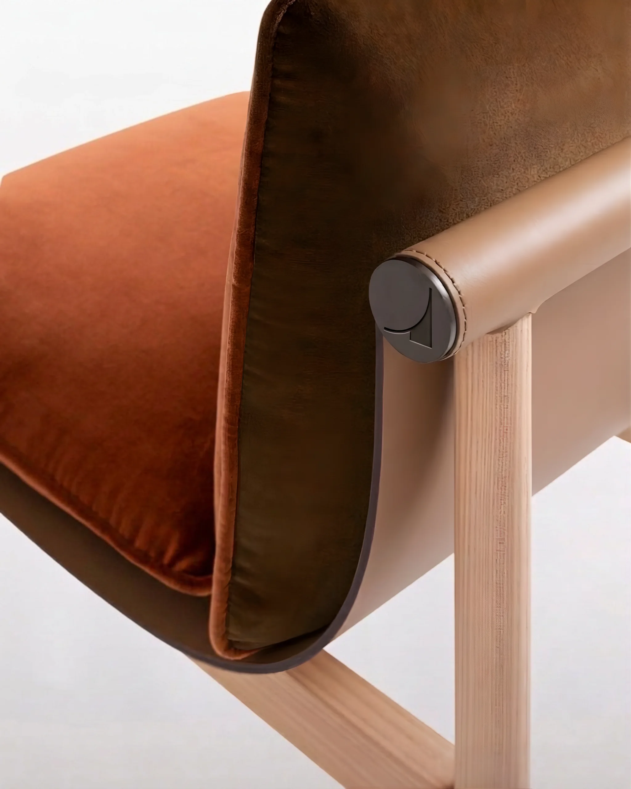 Détail d’un fauteuil avec coussin en velours marron et structure en bois clair et cuir beige.
